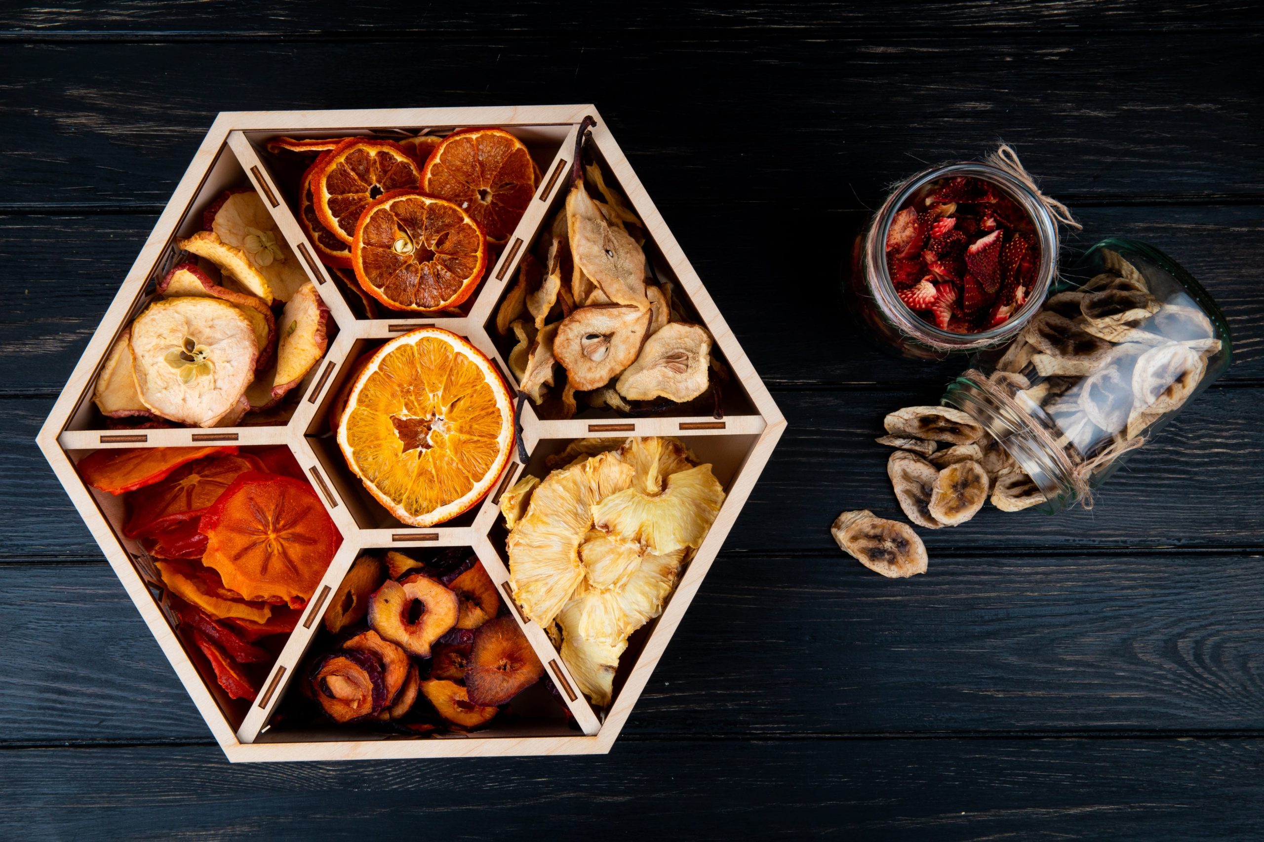 top-view-set-dried-fruits-wooden-box-dried-banana-strawberry-chips-glass-jars-black-background (1)-min